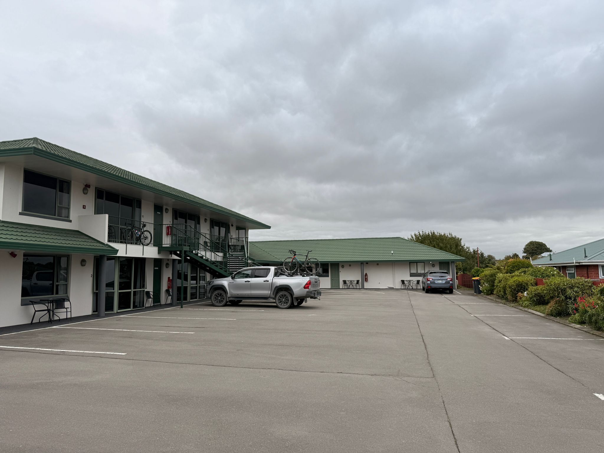 Un motel composé d’un bâtiment à deux étages, d’un espace de stationnement couvert et d’un petit coin salon extérieur.