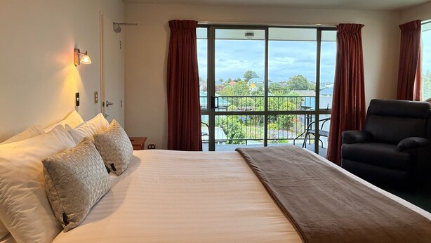 Quarto de hotel com cama grande, uma cadeira, varanda com vista e janela com cortinas.