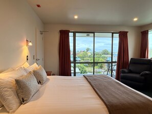 A hotel room with a large bed, a chair, a balcony with a view, and a window with curtains. - Asure Ashley Motor Lodge (Timaru)