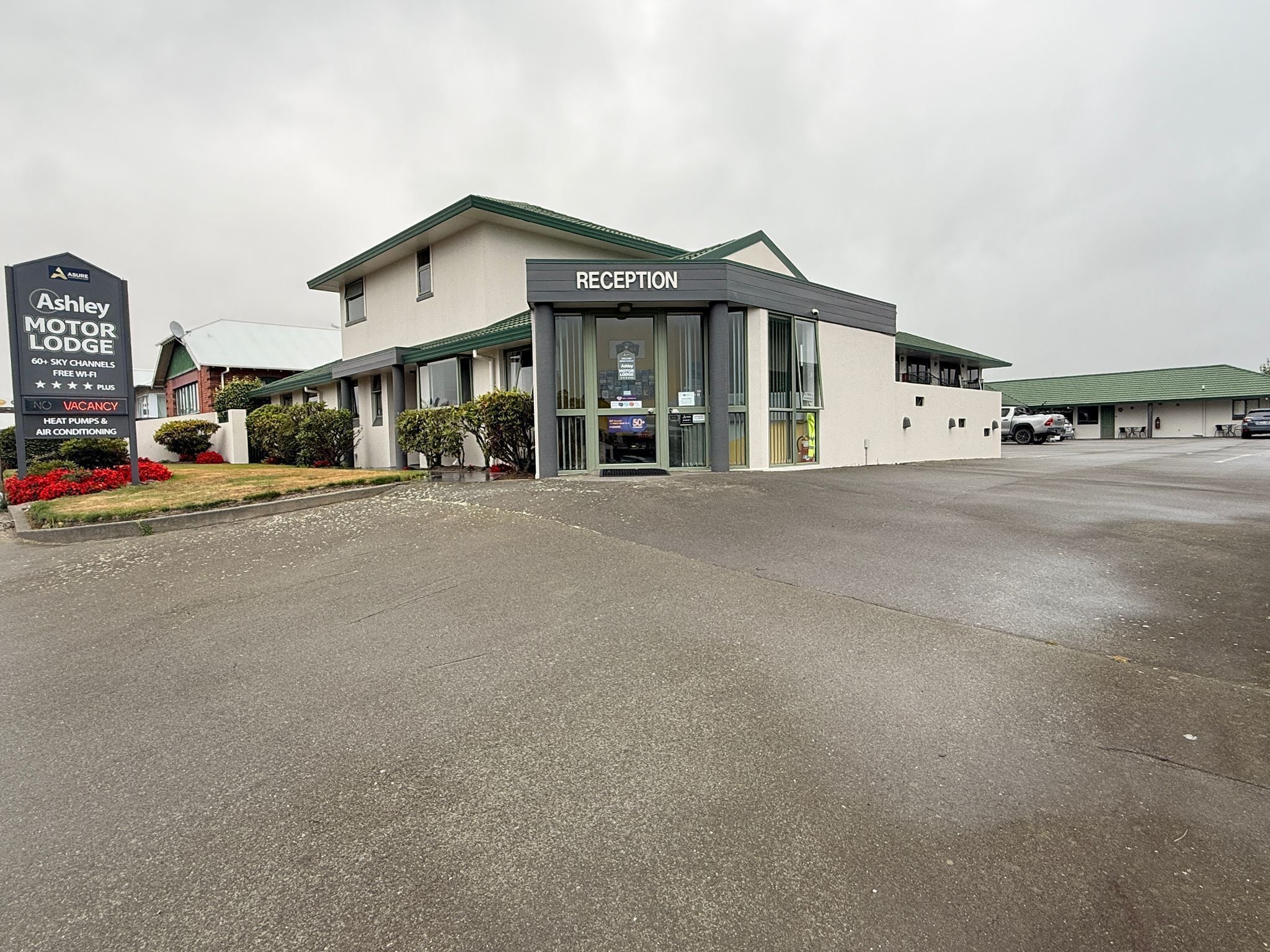 A motel with a reception area, a signboard advertising amenities like 60+ sky channels and free Wi-Fi, and a parking lot.