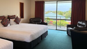 Quarto de hotel com uma cama grande, duas poltronas de couro, uma varanda com vista para edifícios e vegetação.