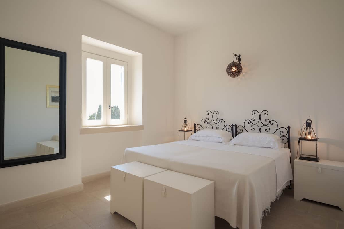Een slaapkamer met een groot bed, nachtkastjes, een spiegel en een raam.