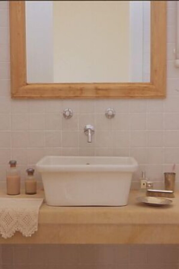 A bathroom with a rectangular sink, two faucets, a mirror with a wooden frame, and a towel on the counter. - Masseria Montelauro (Otranto)