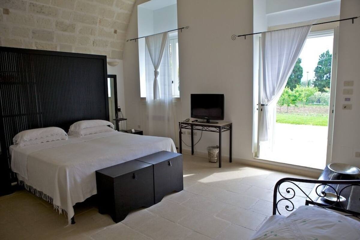 Een slaapkamer met een groot bed, een televisie op een tafeltje en uitzicht op de omgeving door een deur.
