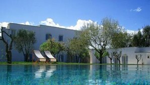 Une piscine à l’eau d’un bleu cristallin, entourée d’arbres et bordée d’un bâtiment blanc doté de nombreuses fenêtres.