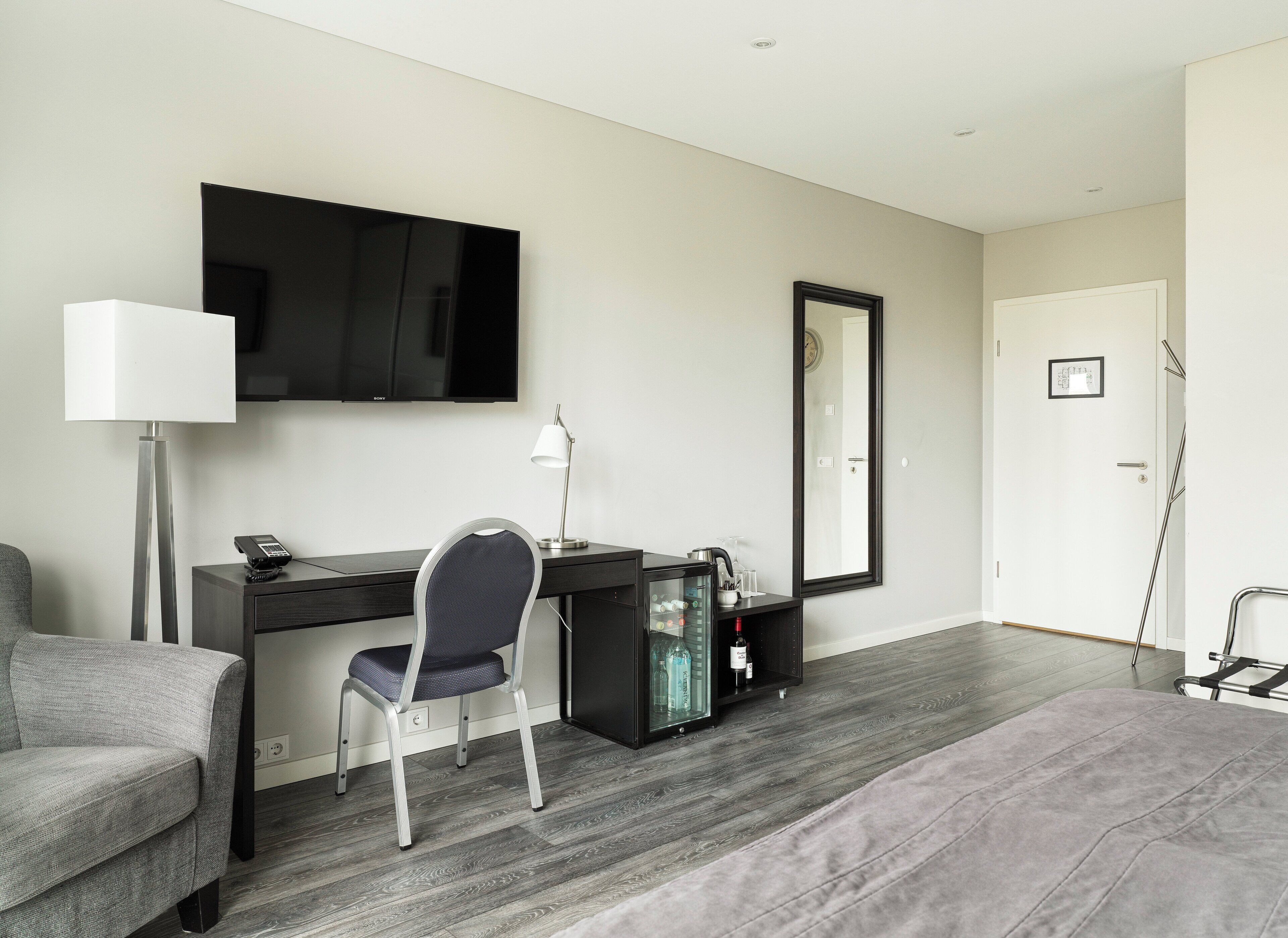 A modern hotel room with a desk, chair, flat-screen TV, and a large mirror.