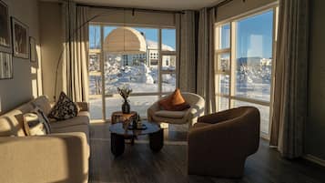 Uma sala de estar moderna com sofá, poltrona e mesa de centro, janelas amplas com vista para a neve e um lustre.
