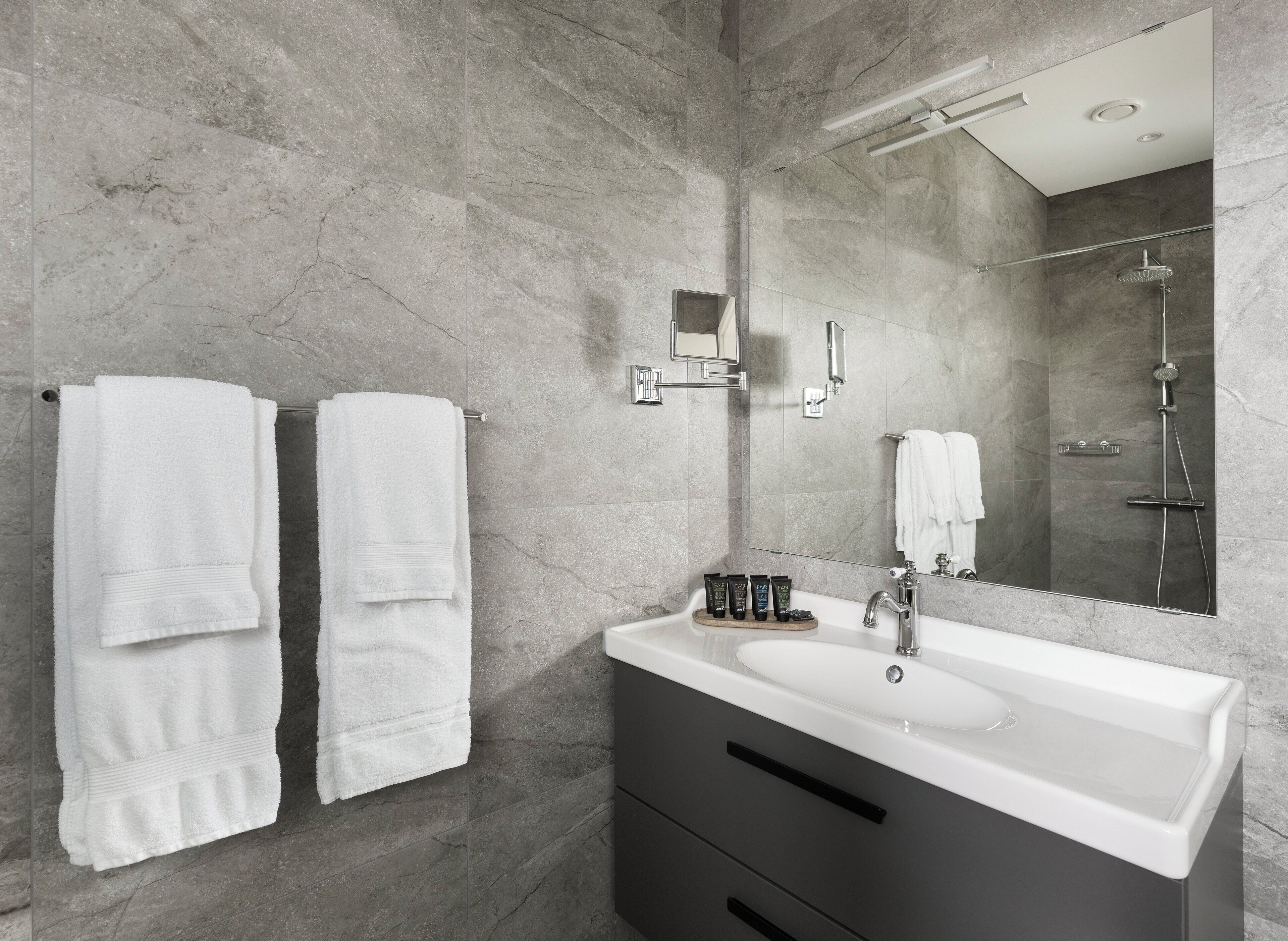 A modern bathroom with a large sink, two towels, a mirror, and a shower.