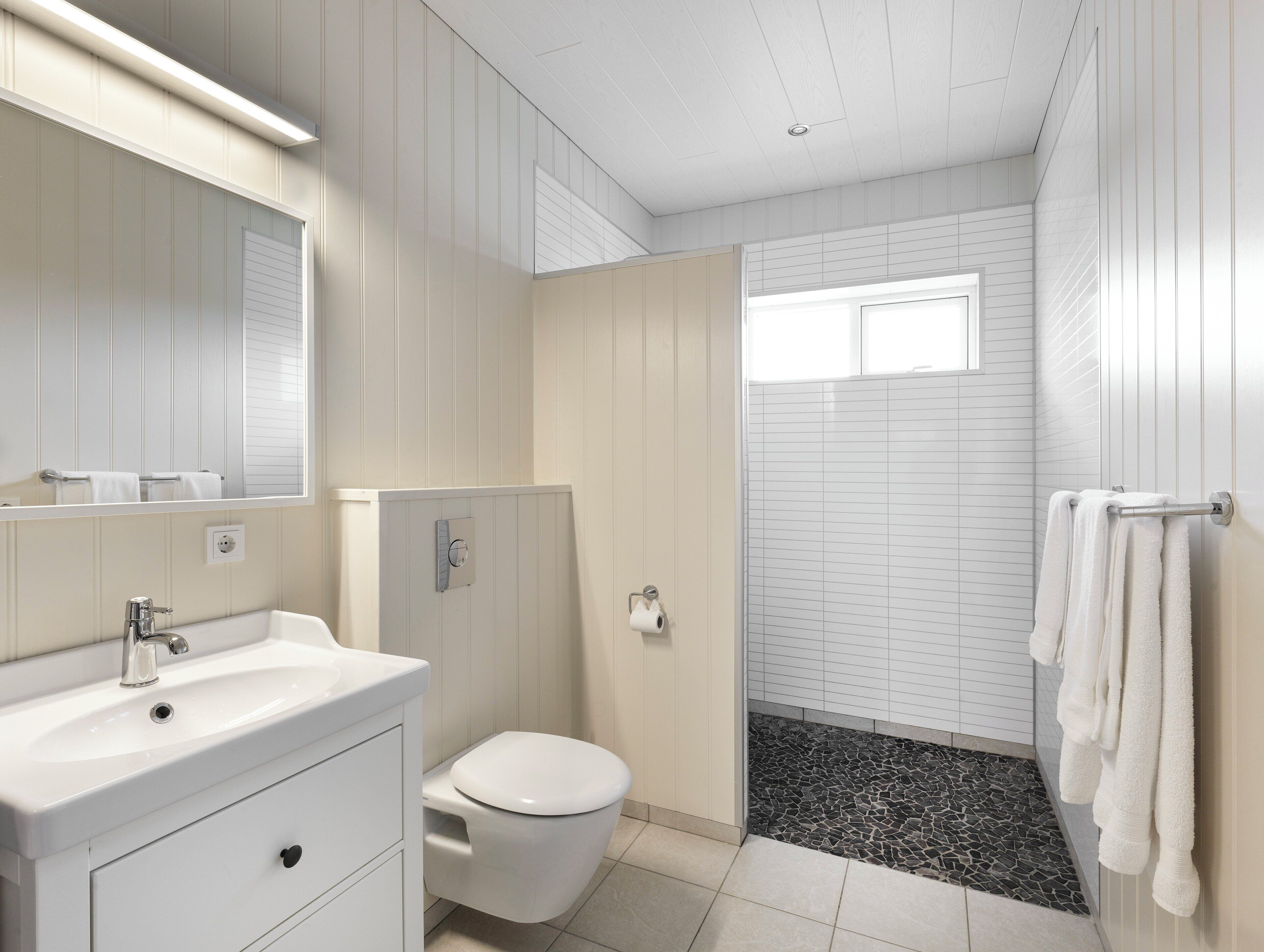 A bathroom with a white vanity, a toilet, a shower with a tiled floor, and a window.