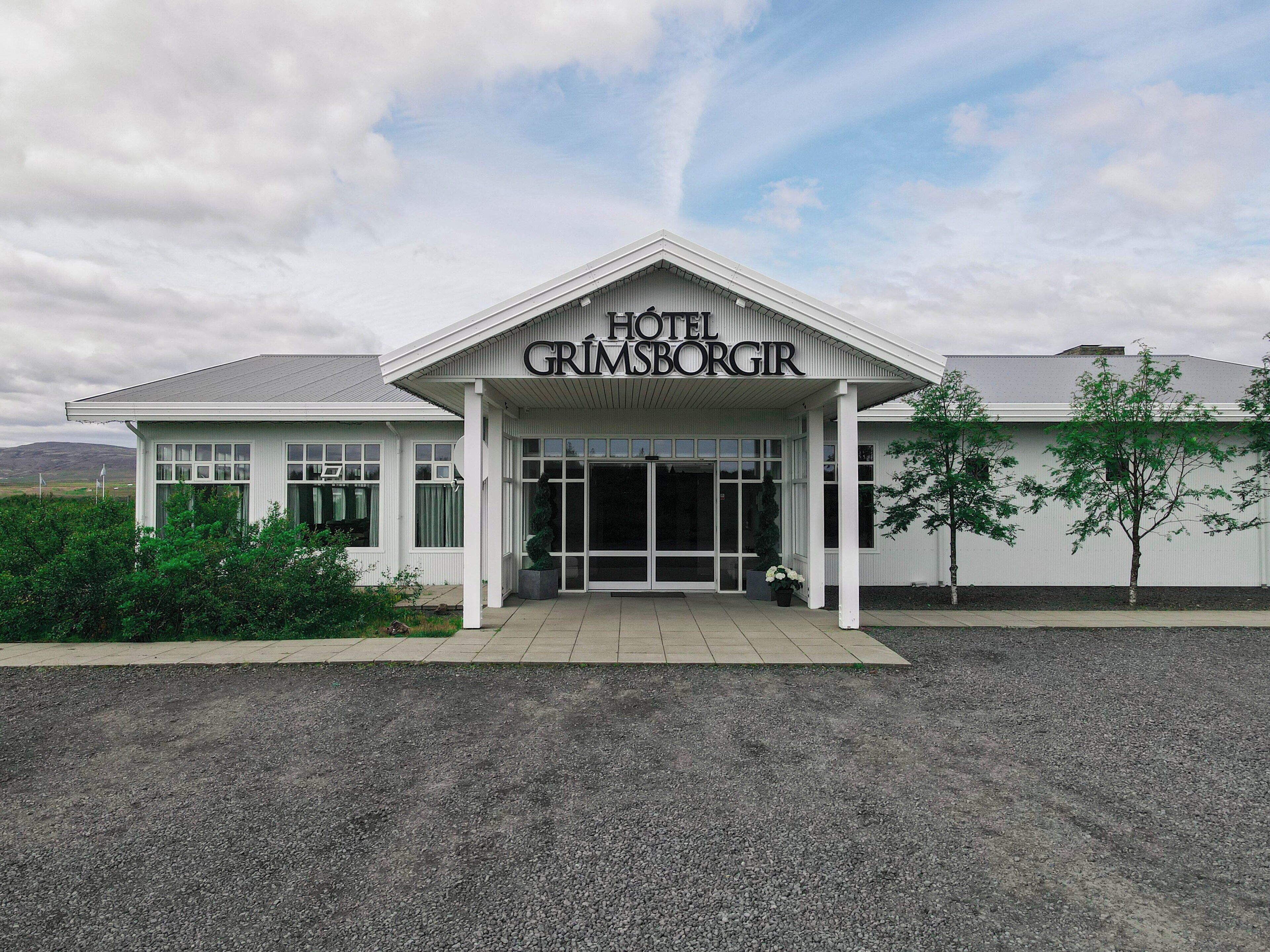 Un hotel llamado 'HOTEL GRIMSBORGIR' con fachada blanca, grandes puertas de entrada y camino de acceso de grava.