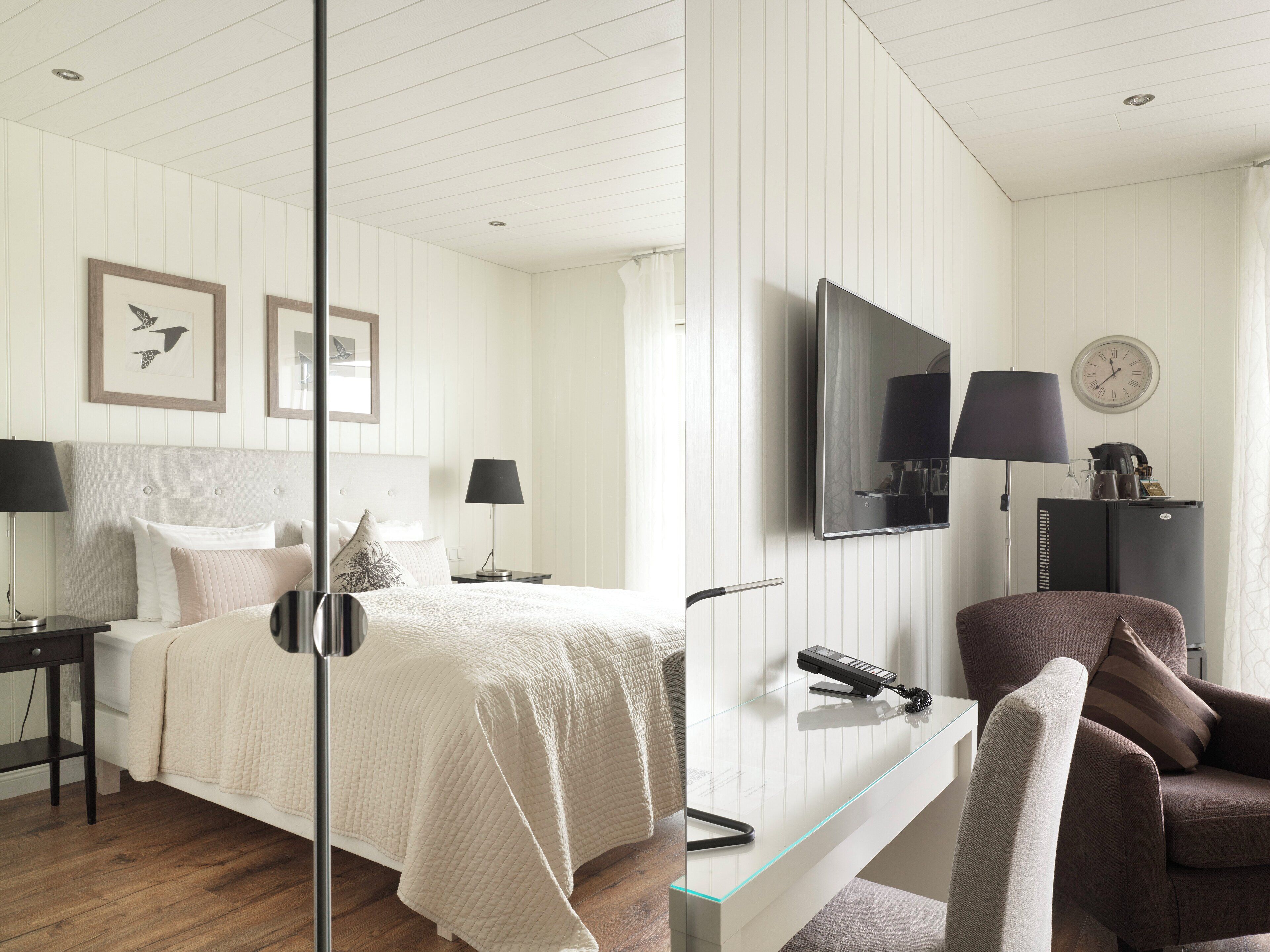 A hotel room with a bed, bedside tables, a desk with a chair, a TV, and a clock on the wall.