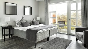 Une chambre moderne avec un grand lit, deux tables de chevet avec des lampes, une grande fenêtre avec des rideaux et une vue sur l’extérieur.