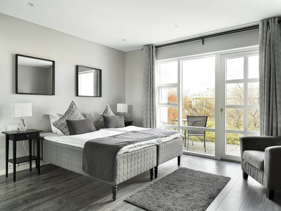 Un dormitorio moderno con una cama grande, dos mesitas de noche con lámparas, un ventanal con cortinas y vistas al exterior.