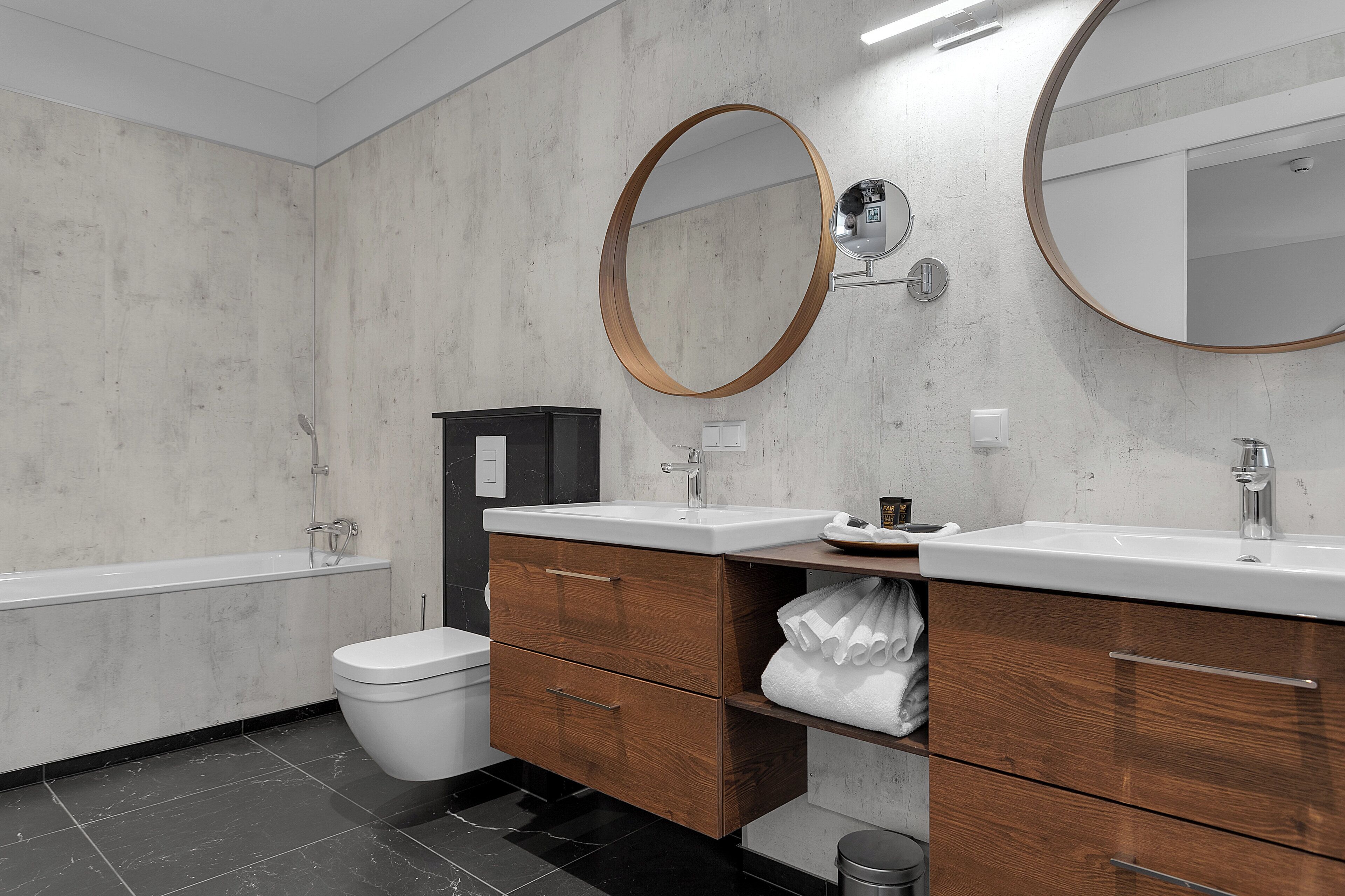 A modern bathroom with a bathtub, a toilet, a vanity with a mirror, and wooden cabinets.