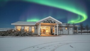 Un hôtel avec une enseigne indiquant « HÔTEL GRIMSBORGIR », un paysage enneigé et des aurores boréales dans le ciel.