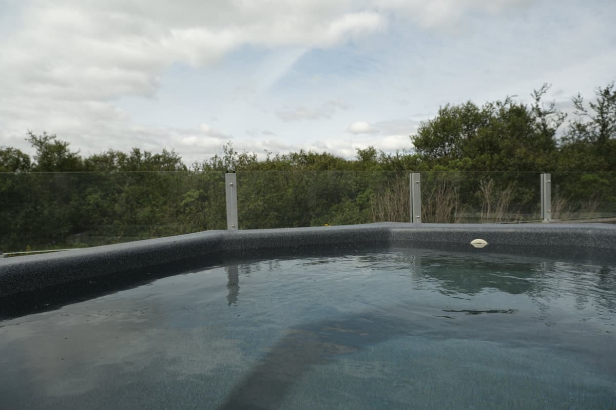 A swimming pool with a curved edge, surrounded by a fence and trees.