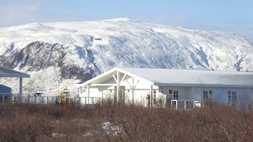 Un edificio con fachada blanca y un espacio exterior cubierto, con montañas nevadas al fondo.