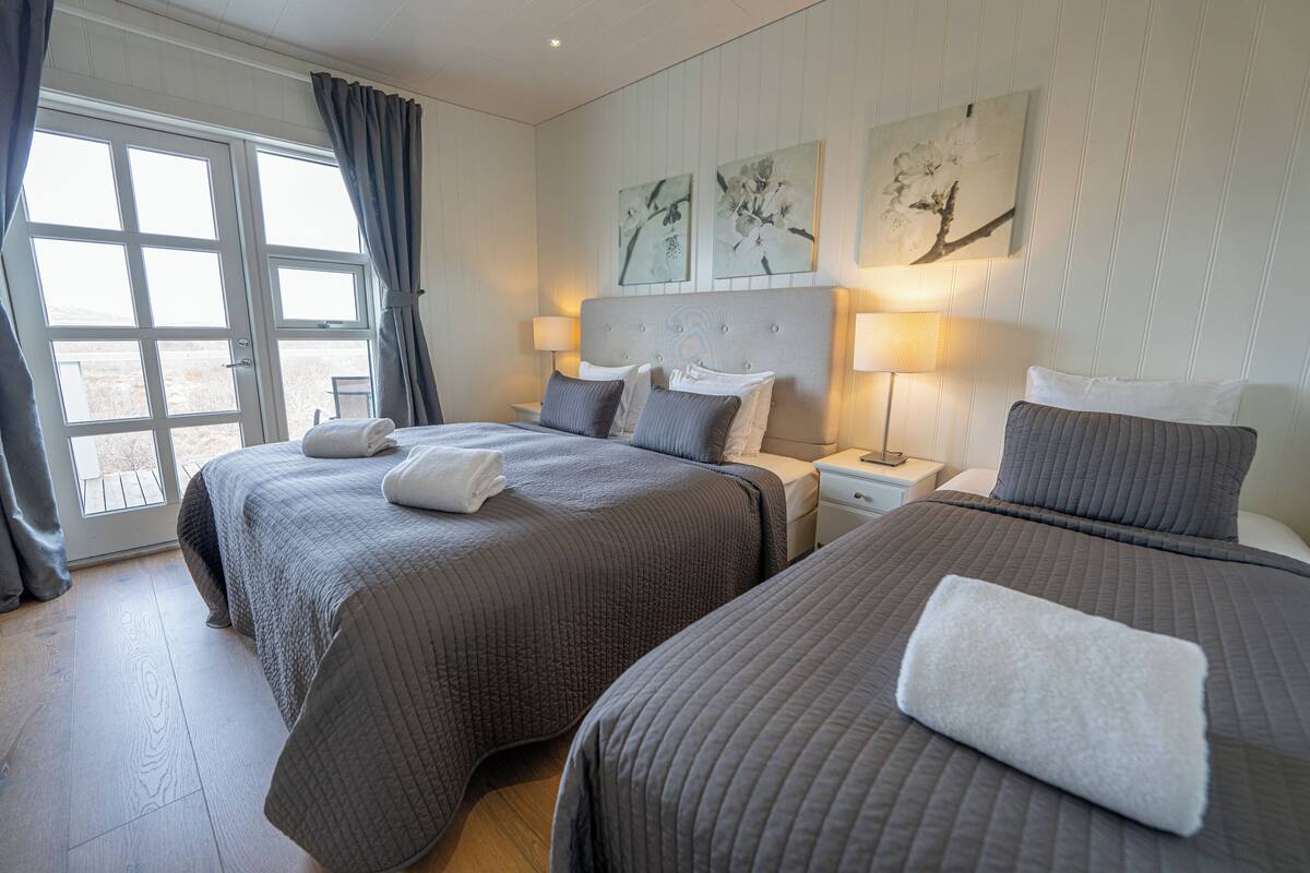 A hotel room with two beds, a large window with curtains, and artwork on the wall.