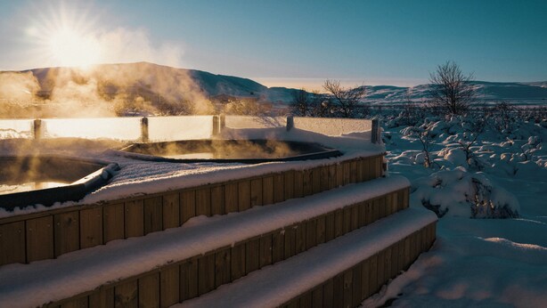 Un bain à remous extérieur en bois, entouré d’escaliers et d’un paysage couverts de neige.