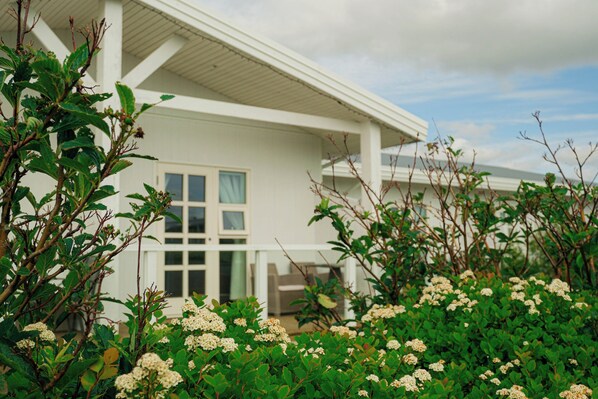 Un bâtiment blanc doté d’un balcon, entouré de verdure et de fleurs blanches.