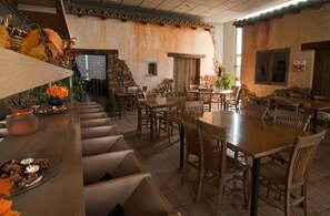 Un comedor rústico con mesas y sillas de madera, paredes de piedra y una variedad de plantas y flores.