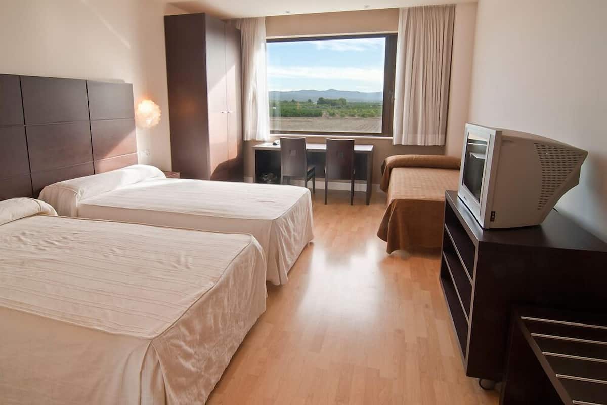 Habitación de hotel con dos camas, un escritorio, un televisor y vistas al exterior.