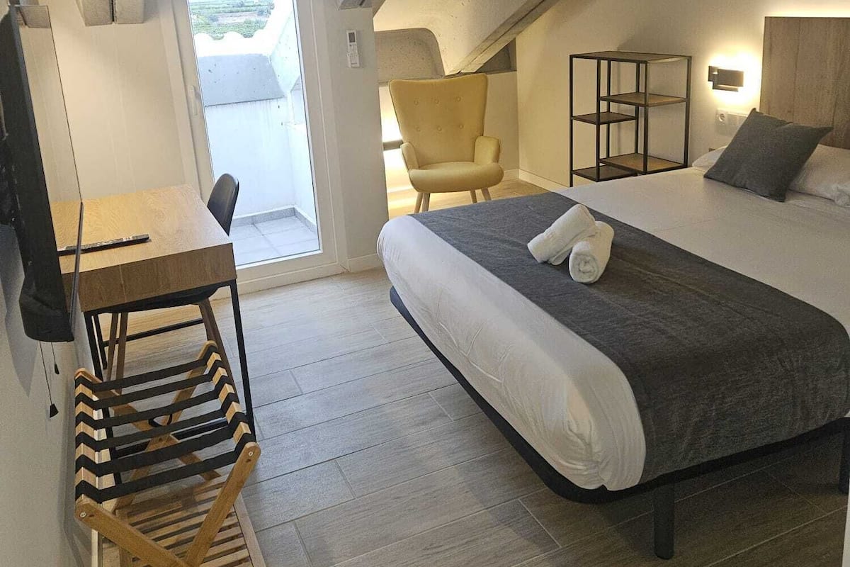 Una habitación compacta con cama, una silla, un escritorio y una mesita.