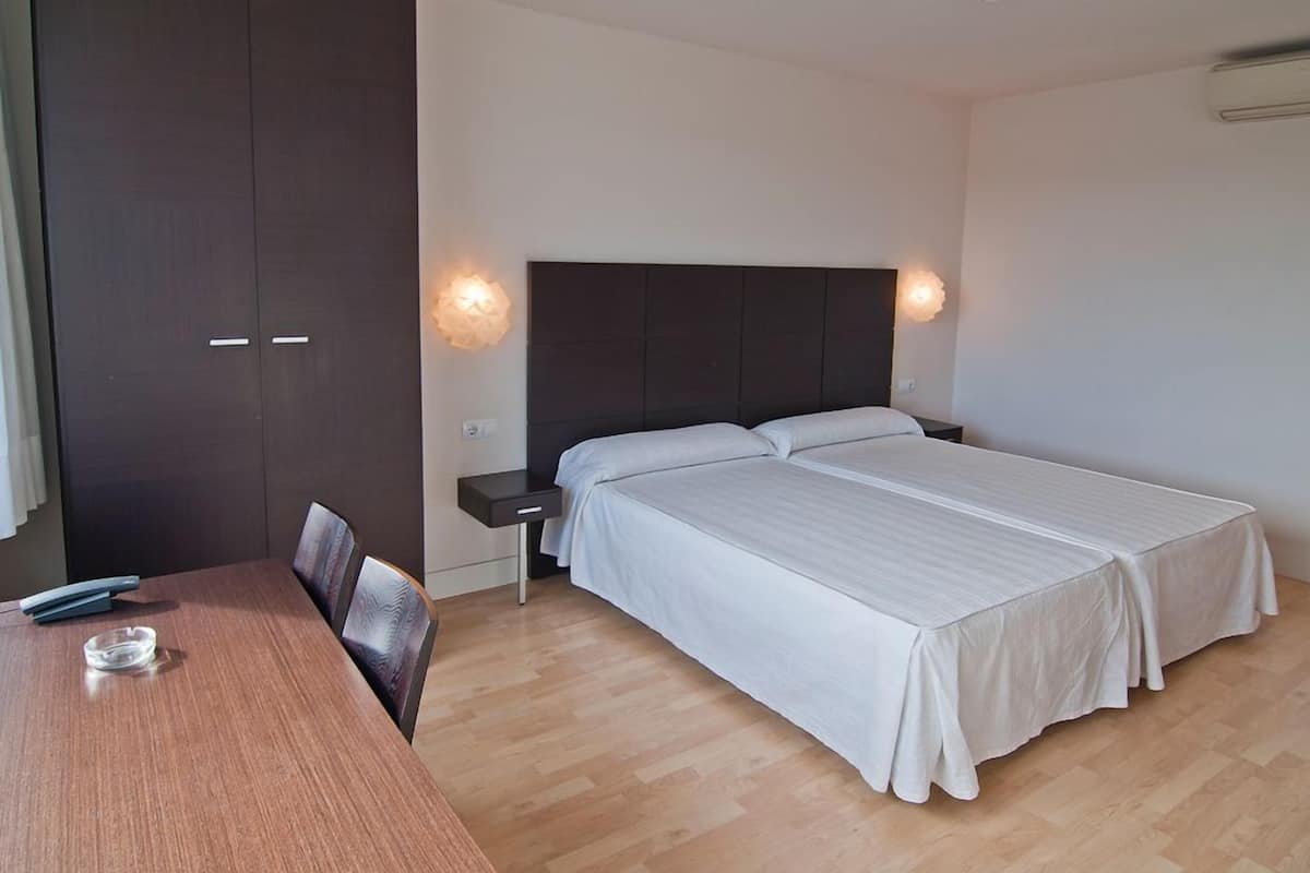 Un dormitorio con una cama doble, una mesita de noche, un escritorio de madera y una silla.