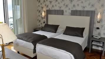 Habitación de hotel con dos camas, una mesita de noche con lámpara y vista al exterior.