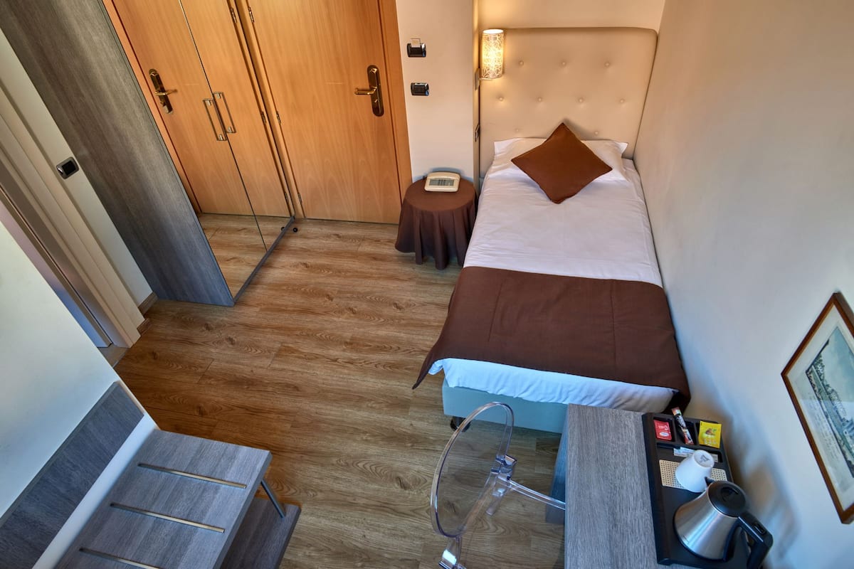 A compact hotel room with a bed, bedside table, and a small desk with a chair.