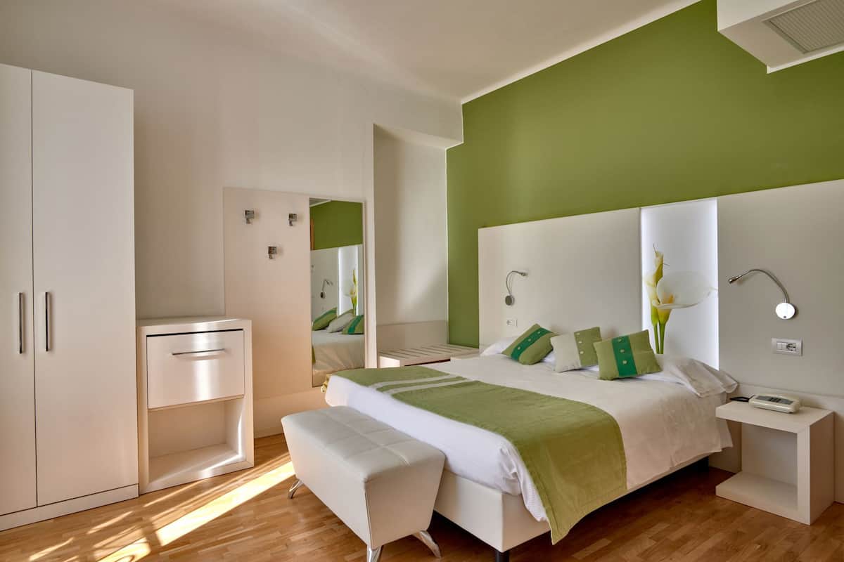 A modern bedroom with a bed, bedside tables, a wardrobe, and a mirror.