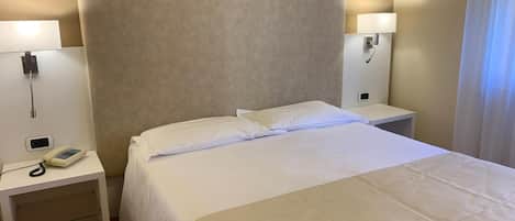 A hotel room with a large bed, two bedside tables, a lamp on each table, and a telephone on one of the tables.