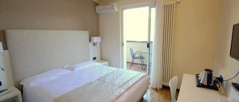 Een hotelkamer met een groot bed, een bureau met koffiezetapparaat, een airconditioner en uitzicht op het balkon.