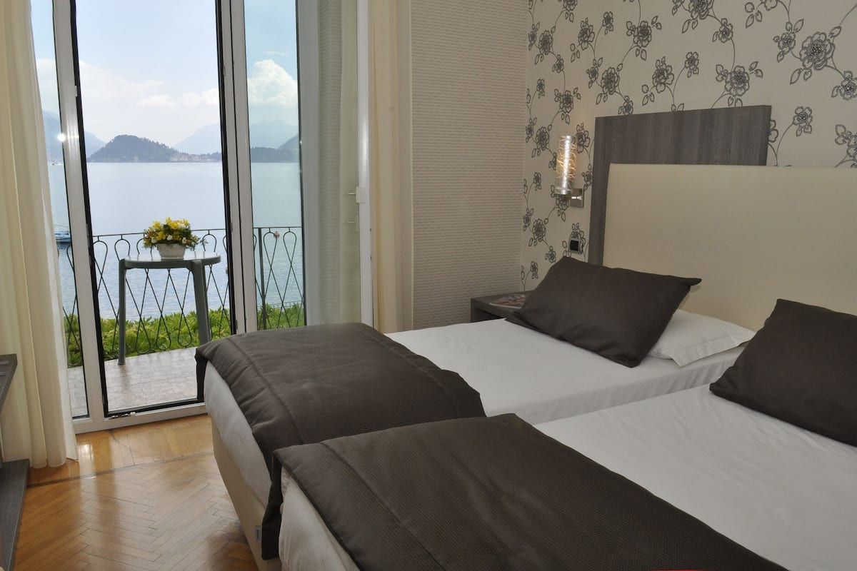 A bedroom with two beds, a view of a lake, and a balcony with a table and flowers.
