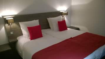 A neatly made double bed with white bedding and two red pillows, flanked by nightstands with lamps.