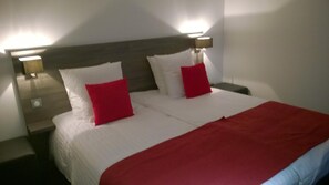 A neatly made double bed with white bedding and two red pillows, flanked by nightstands with lamps. - Cour du Tonnelier (Bouxwiller)