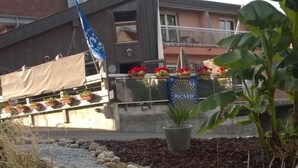 Un sendero en un jardín con piedras y plantas, un cartel de cerveza Ricard y un edificio con balcones al fondo.