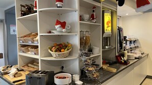 Zona de desayuno tipo bufé con estantes de pan, una cesta de fruta, una máquina de café y un tostador.