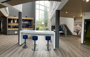 Un área de bar moderna con una barra blanca, dos taburetes azules y un amplio ventanal con vistas al exterior.