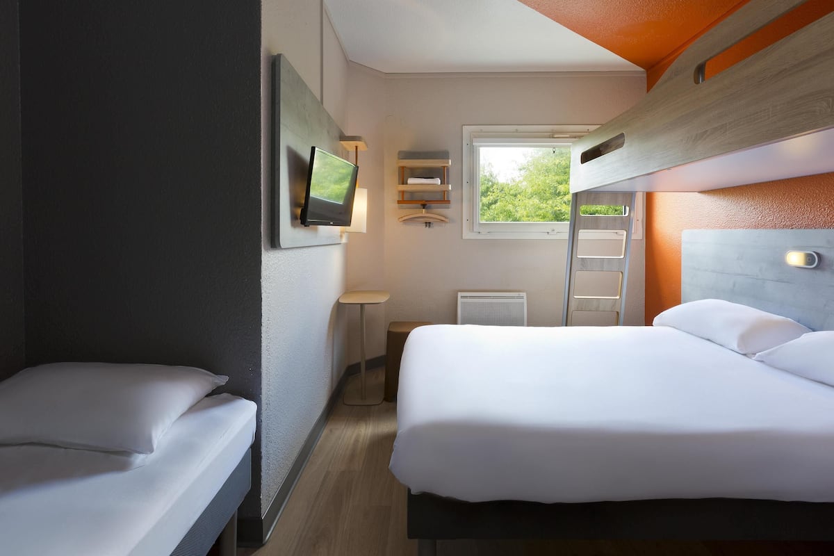 A compact hotel room with two beds, a television, a window, and a ladder.