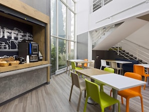 Un interior moderno con una estación de café, mesas, sillas y una escalera.