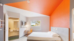 A bedroom with a bed, a TV, a window, and a bathroom visible through an open door. - ibis budget Le Mans Universite (Le Mans)