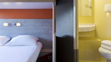 A hotel room with a bed, a wooden headboard, a bathroom with a yellow wall, a sink, and a toilet.