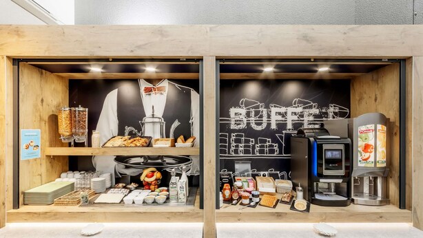 A breakfast bar with a coffee machine, a fruit display, and a chalkboard menu. - ibis budget Le Mans Universite (Le Mans)