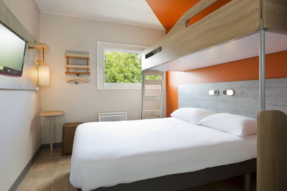 Habitación con literas, televisión, lámpara de noche, ventana y una mesita pequeña.