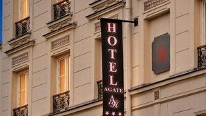 Un cartel de hotel con la leyenda 'HOTEL AGATE' y un logotipo, adherido a un edificio con varias ventanas y balcones.