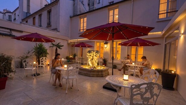 Un patio al aire libre con mesas, sillas, sombrillas y una fuente.
