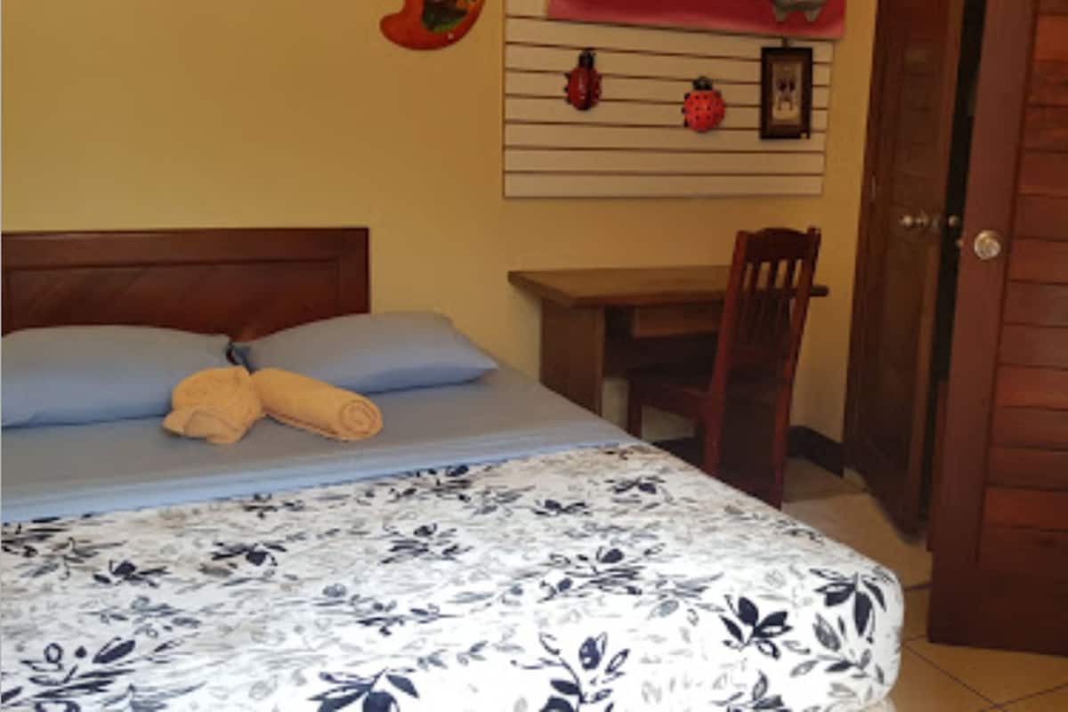 A bed with a floral bedspread, a wooden headboard, two rolled towels, and a blue pillow.
