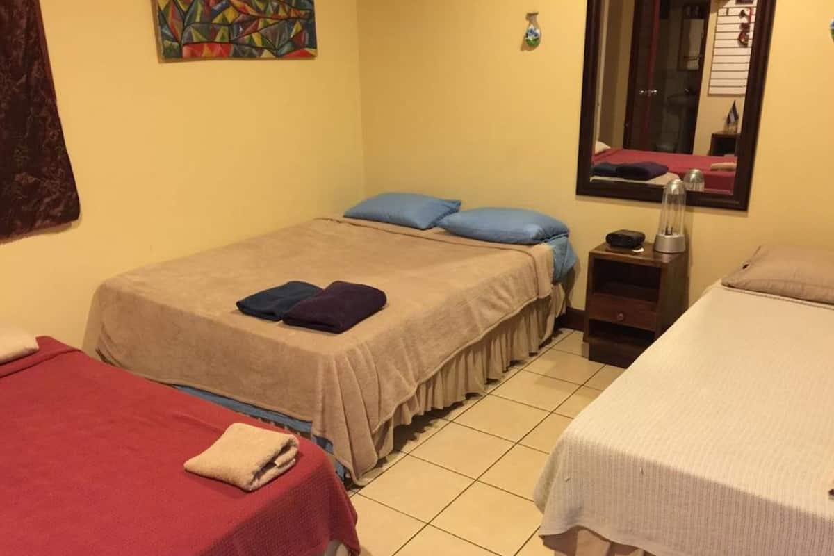 A hotel room with two beds, a small bedside table with a lamp, and a window with a mirror.