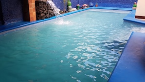 Una piscina con agua cristalina, una cascada y elementos decorativos como hongos y una rana.